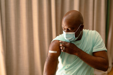 Portrait of african american senior man in face mask showing plaster after vaccination