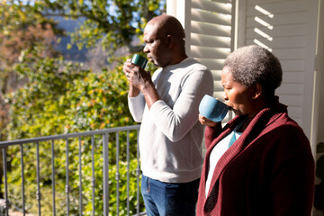 African american senior couple drinking coffee standing on balcony and looking into distance