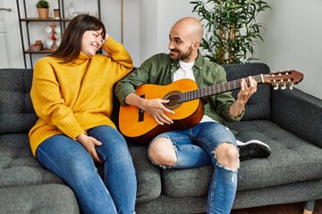 Young hispanic couple smiling happy playing classical guitar sitting on the sofa at home.