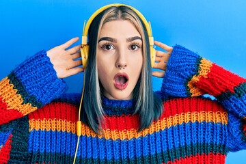 Young modern girl listening to music using headphones afraid and shocked with surprise and amazed...