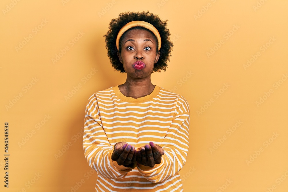 Poster Young african american woman holding hands together cupped, giving concept puffing cheeks with funny face. mouth inflated with air, catching air.