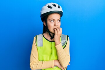 Beautiful brunette little girl wearing bike helmet and reflective vest looking stressed and nervous with hands on mouth biting nails. anxiety problem.
