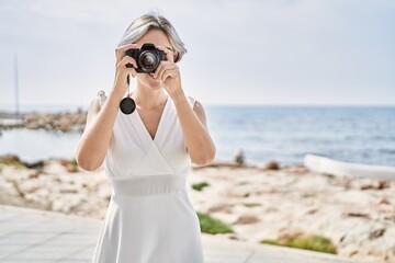 Young caucasian girl smiling happy using professional camera at the beach.