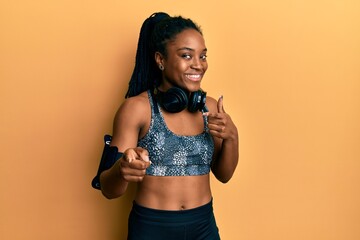 Fototapeta na wymiar African american woman with braided hair wearing sportswear and arm band pointing fingers to camera with happy and funny face. good energy and vibes.