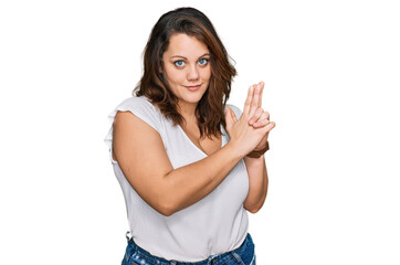 Young plus size woman wearing casual white t shirt holding symbolic gun with hand gesture, playing killing shooting weapons, angry face