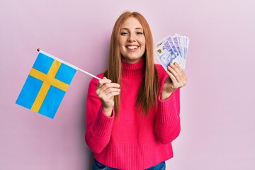 Young irish woman holding sweden flag and krone banknotes smiling and laughing hard out loud because funny crazy joke.