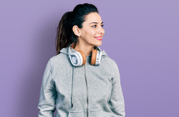 Young hispanic woman wearing gym clothes and using headphones looking to side, relax profile pose with natural face and confident smile.