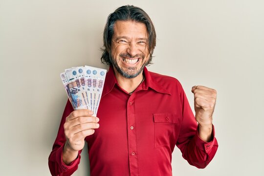 Middle age handsome man holding russian 500 ruble banknotes screaming proud, celebrating victory and success very excited with raised arm
