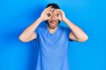 Middle age caucasian man wearing casual clothes doing ok gesture like binoculars sticking tongue out, eyes looking through fingers. crazy expression.