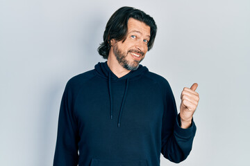 Middle age caucasian man wearing casual sweatshirt smiling with happy face looking and pointing to the side with thumb up.