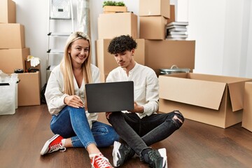 Young beautiful couple smiling happy using laptop at new home.