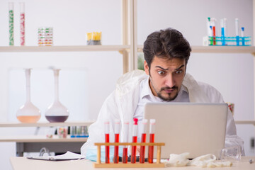 Young male chemist sitting at computer at the lab