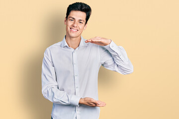 Young hispanic business man wearing business clothes gesturing with hands showing big and large size sign, measure symbol. smiling looking at the camera. measuring concept.