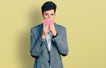 Young hispanic business man covering face with cards clueless and confused expression. doubt concept.