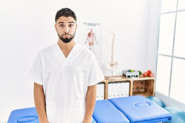 Obraz premium Young handsome man with beard working at pain recovery clinic puffing cheeks with funny face. mouth inflated with air, crazy expression.