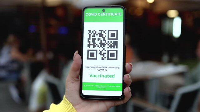 Hand holding digital green pass certificate for coronavirus vaccine with bar restaurant on background