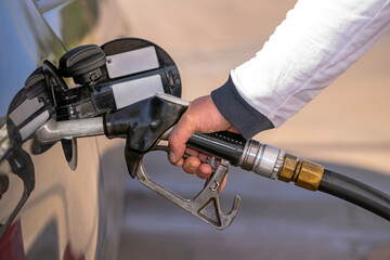 MALE HAND HOLDING FUEL DISPENSER NOZZLE AND REFILLING A CAR IN THE GAS STATION.