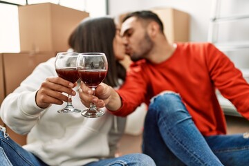 Young latin couple kissing and toasting with red wine at new home