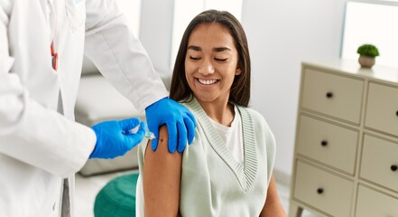 Doctor injecting covid-19 vaccine to latin woman at clinic.