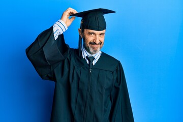 Middle age hispanic man wearing graduation cap and ceremony robe confuse and wonder about question. uncertain with doubt, thinking with hand on head. pensive concept. - Powered by Adobe