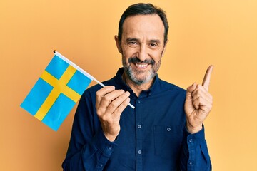 Middle age hispanic man holding sweden flag smiling happy pointing with hand and finger to the side