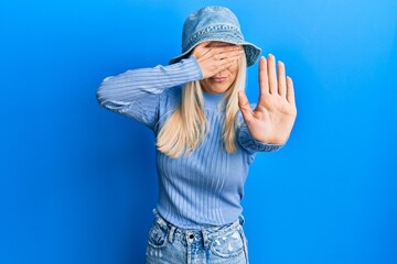Young blonde woman wearing casual denim hat covering eyes with hands and doing stop gesture with sad and fear expression. embarrassed and negative concept.