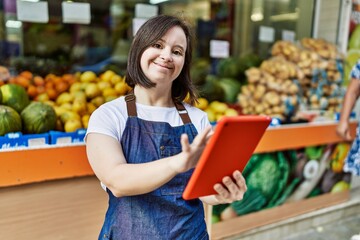 Young down syndrome woman wearing apron using touchpad at fruit store
