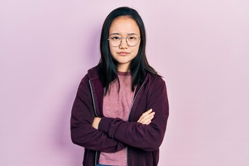 Young chinese girl wearing casual clothes and glasses skeptic and nervous, disapproving expression on face with crossed arms. negative person.