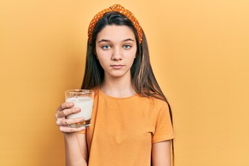 Young brunette girl drinking a glass of milk thinking attitude and sober expression looking self confident