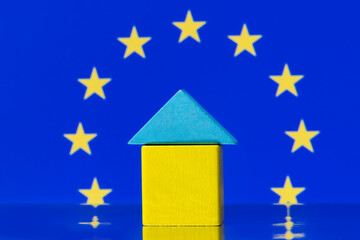 Small wooden house made of children's cubes against the background of the flag of the European Union