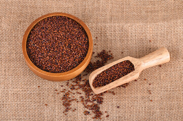 Red quinoa grains in a wooden bowl and spoon isolated on sack background
