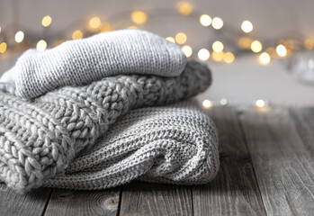 Fototapeta na wymiar Cozy winter background with a stack of knitted sweaters and lights, copy space.