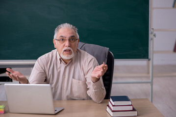 Old male teacher in front of blackboard