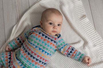 portrait of a newborn baby in a colored bodysuit lying on his back on a knitted white blanket made of natural cotton. top view. space for text. High quality photo