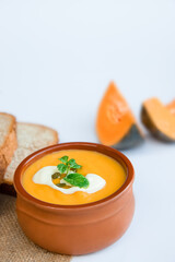 yellow pumpkin soup served and ready with bread, two pieces of raw pumkin in the background, thanksgiving or winter meal, traditional autumn food. 
