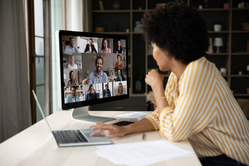 Back rear side view happy young african american woman employee looking at computer monitor, holding online video call talk or distant negotiations meeting with diverse colleagues, working from home.