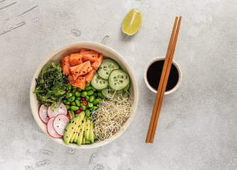 Healthy poke bowl with salmon, avocado, edamame beans, cucumber, radish, and seaweed, top view....