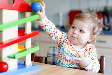 Fototapeta na wymiar Little baby girl playing with educational toys at home or nursery. Happy healthy toddler child having fun with colorful wooden toy ball track. Kid learning to hold and roll balls. Motoric education.