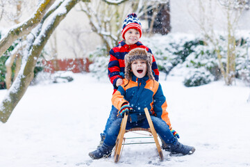 Fototapeta na wymiar Two kid boys having fun sleigh ride during snowfall. Children sledding on snow. siblings riding a sledge. Twins play outdoors. Friends sled in snowy winter park. Active fun for family vacation