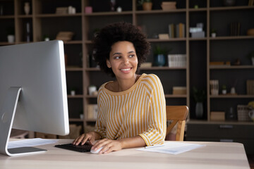 Thoughtful smiling young african american business lady working on computer in modern home office,...