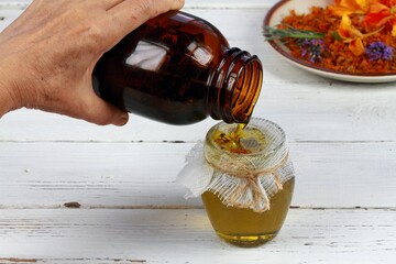 Herbal oil, woman filtering medicinal herbs.  Hand holding bottle with oil and herbs. Homemade curative oil good for the skin.