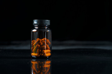 A dark transparent bottle of medicine stands on a black mirrored table.
