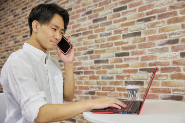 電話しながらノートパソコンを触る日本人男性