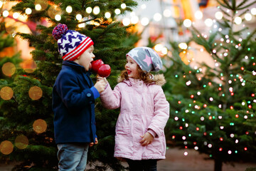 Two little smiling kids, preschool boy and girl eat sweet sugared apple on German Christmas market....
