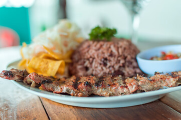 Roast beef with gallo pinto and pico de gallo,  Plate with roast beef and rice served on wooden table. Nicaraguan food served on wooden table