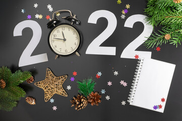 Layout on the theme of the New Year 2022 with numbers, clocks, toys and branches of a Christmas tree on a dark background.
