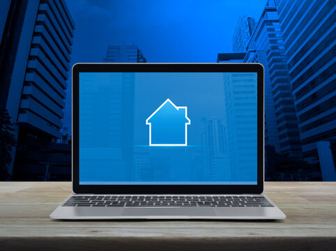 House icon with copy space on modern laptop computer monitor screen on wooden table over office city tower and skyscraper, Business real estate online concept