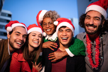 Group of smiling multiracial friends wearing Santa Claus hats looking at camera celebrate Christmas together.