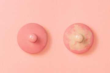 Two pink ceramic lids on a pink background symbolizing the female breast. Right side lid dirtied. Flat lay. Copy space. Concept of Breast Cancer Awareness Month