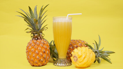 pineapple fruit and a glass of juice isolated on a yellow background